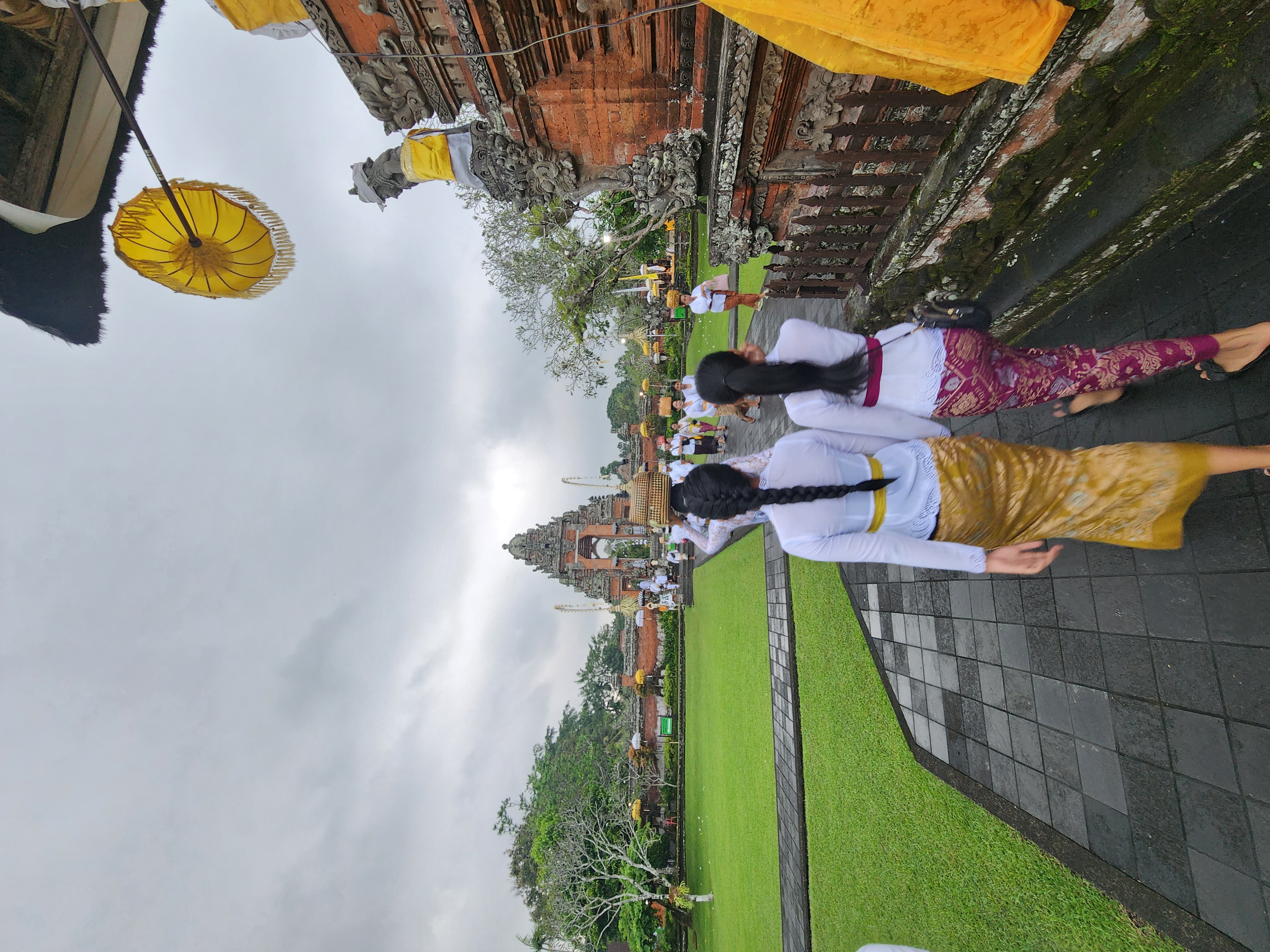 Women in kebaya and sarongs walking toward a carved stone temple gateway in Bali