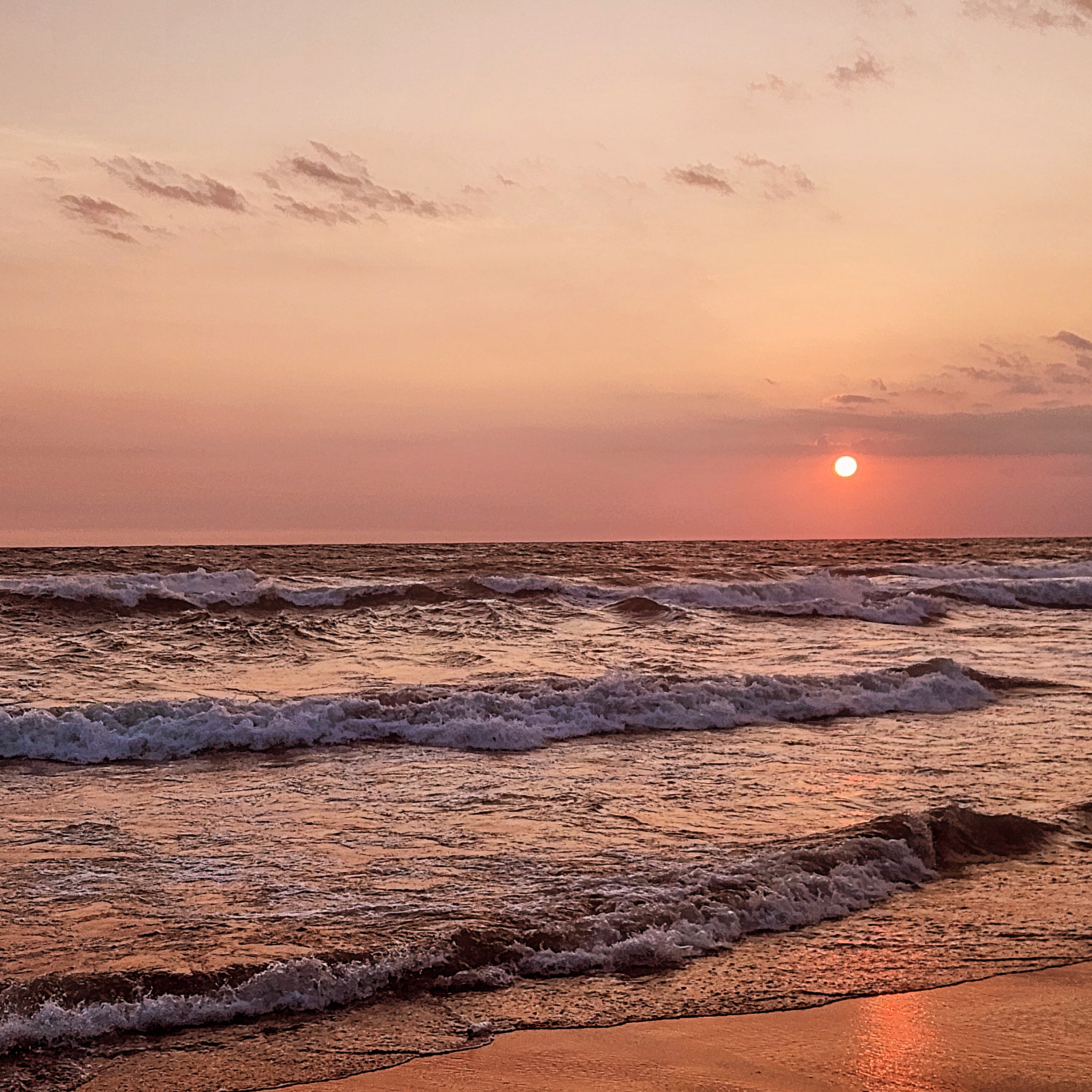 Sun low over the ocean at a Balinese beach, waves and wet sand reflecting orange light