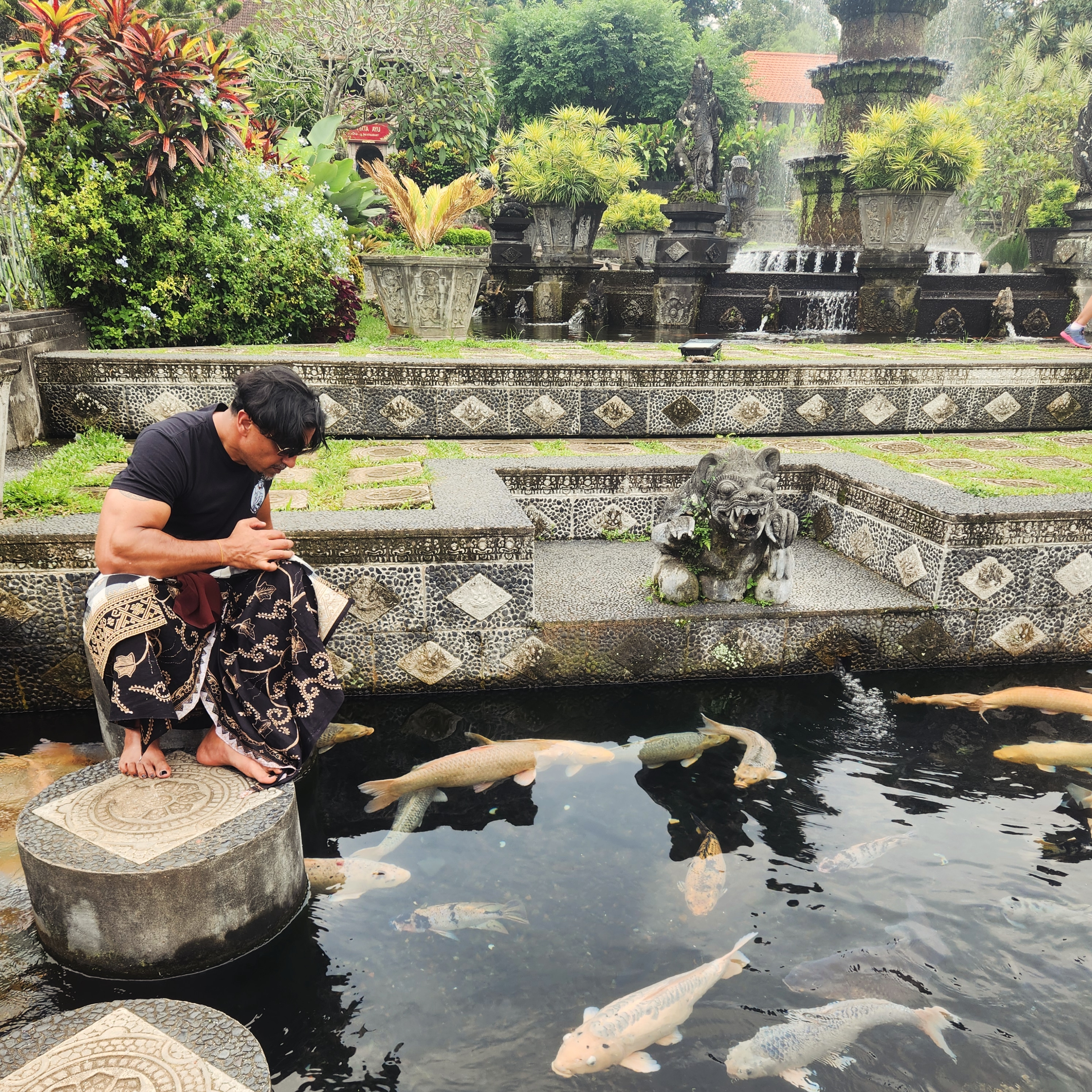 Man in sarong with hands joined in prayer beside a koi pond in a Balinese garden